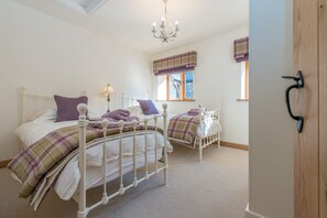 Een slaapkamer met twee bedden, een kroonluchter en ruitpatroon gordijnen.