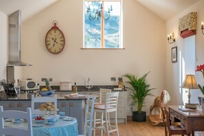 Una cocina con un reloj, una ventana y un comedor con sillas y una mesa.