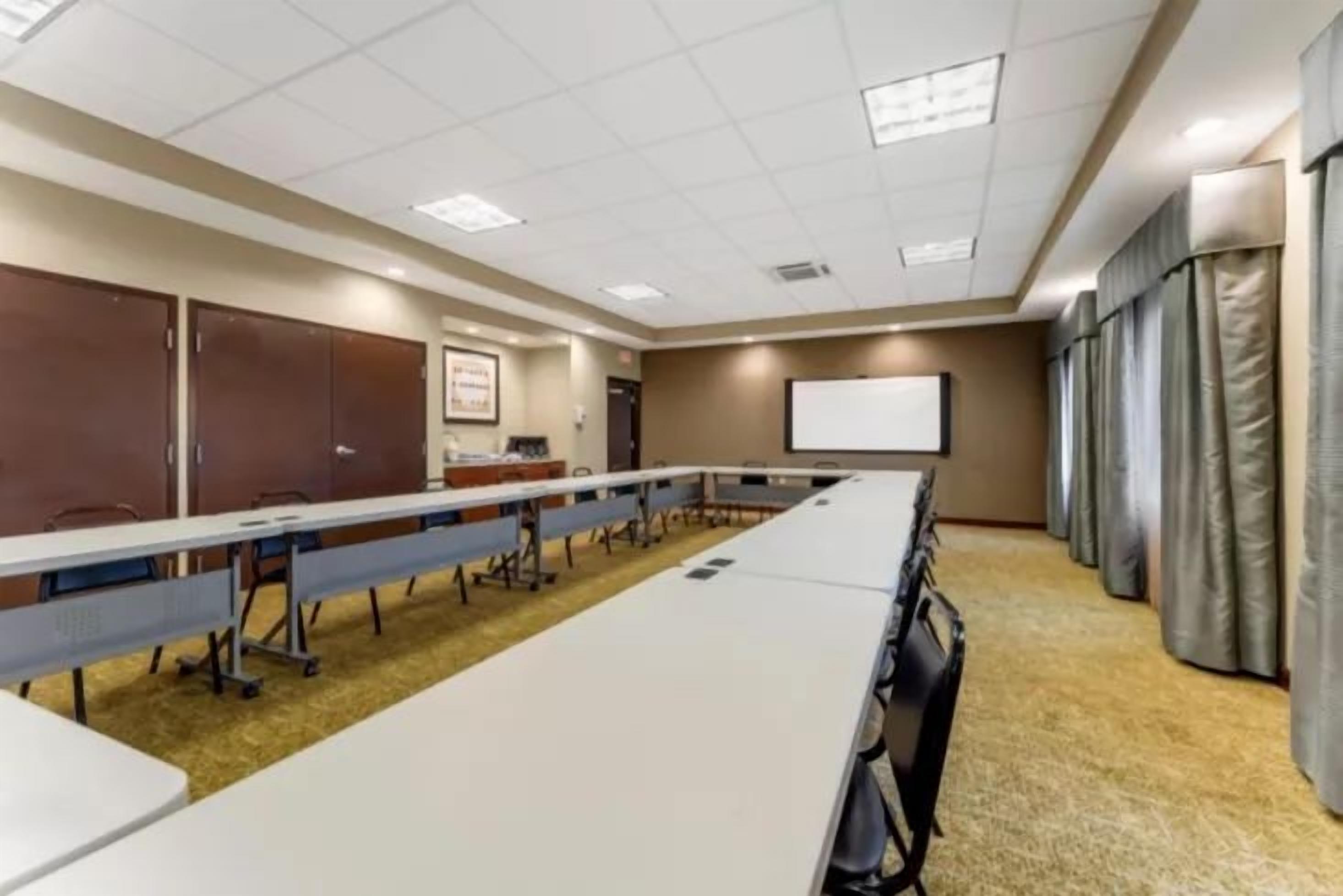 Une salle de conférence équipée d’une longue table, de chaises, d’un écran de projection et d’un tableau blanc.