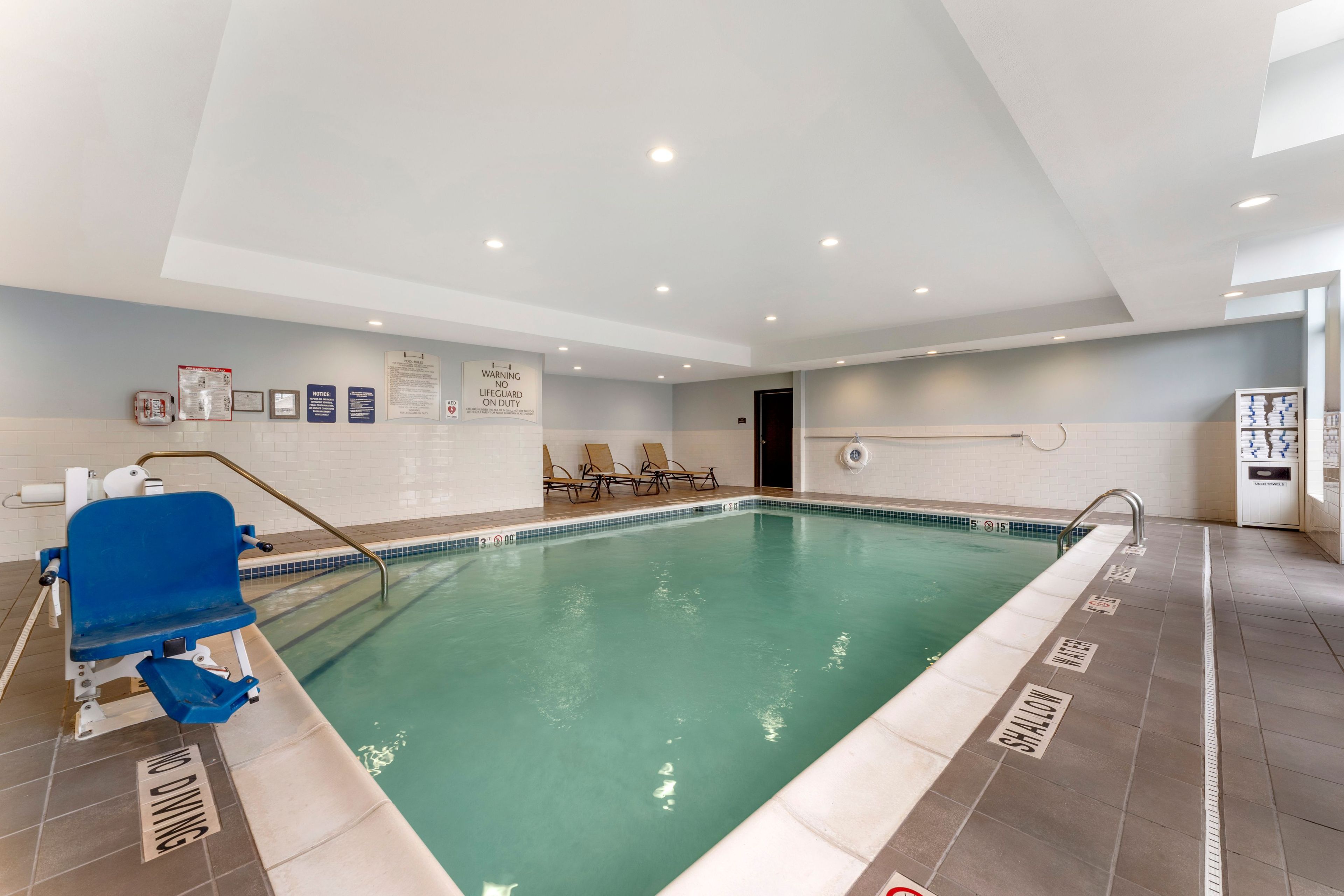 Ein Hallenbad mit Rettungsschwimmerstuhl, Liegestühlen und Sicherheitsschildern.