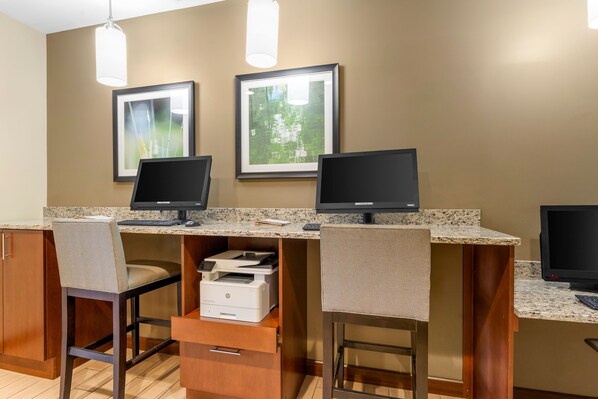 Un espace de travail équipé de trois postes informatiques, chacun comprenant un écran, un clavier et une imprimante. Deux tableaux encadrés ornent le mur, et la pièce est dotée de meubles en bois et d’un plan de travail.
