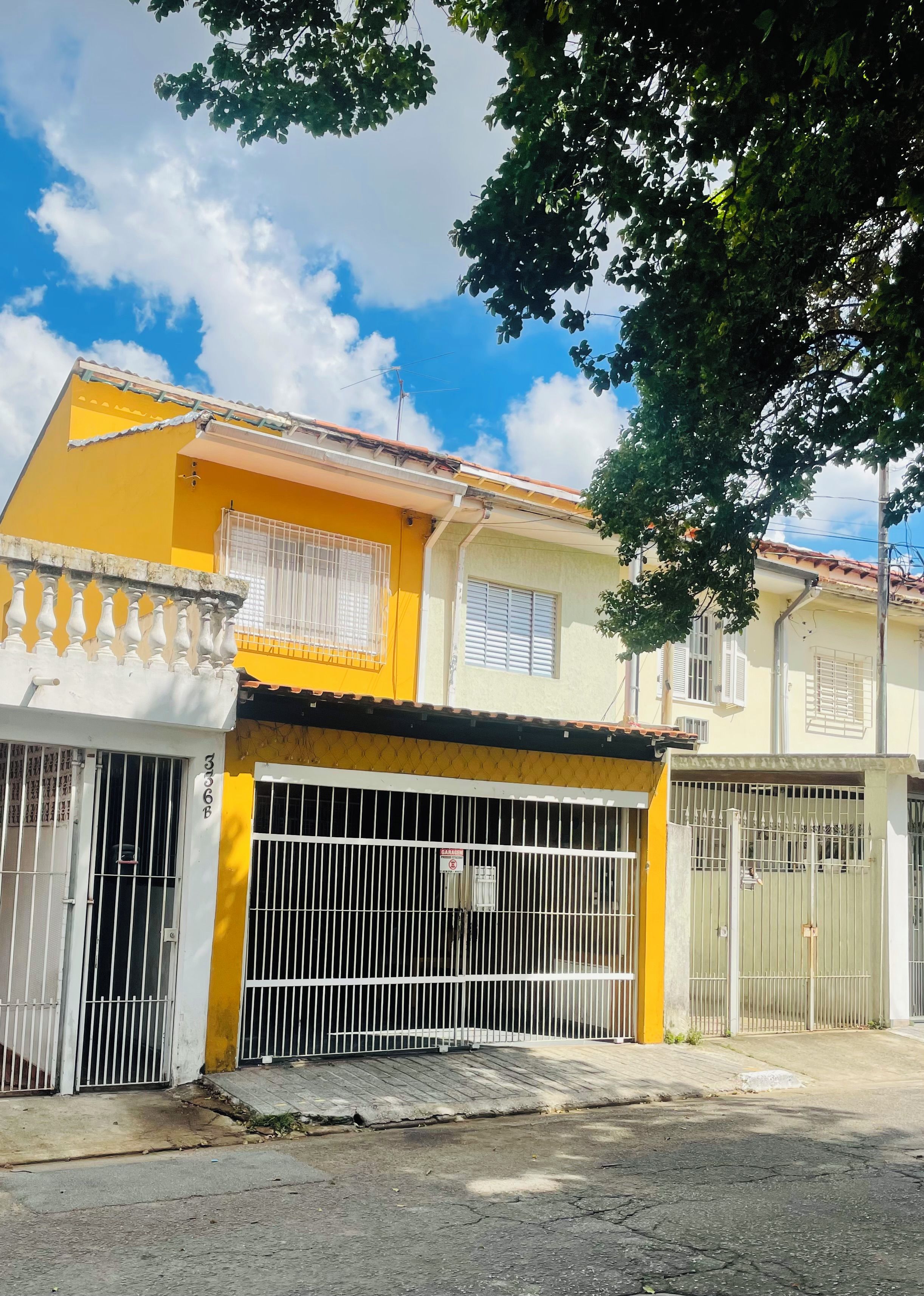 Edifício residencial com fachada amarela, entrada com portão e varanda visível.