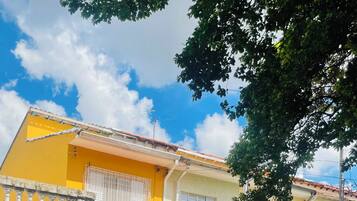 Edifício residencial com fachada amarela, entrada com portão e varanda visível.
