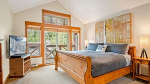 Quarto com cama de madeira, televisão, um quadro e vista para o exterior.
