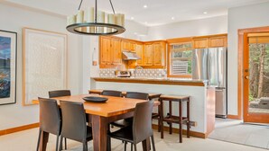 Cozinha moderna com armários de madeira, uma ilha central e uma área de refeições com mesa e cadeiras.