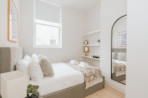 Un dormitorio con cama, mesita de noche, espejo y ventana.