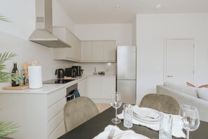A modern kitchen with white cabinetry, a dining table set for two, and a refrigerator. - Premium London Stay – Luxury 1-Bed Apartment (London)