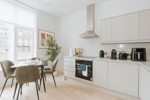 Una cocina moderna con armarios blancos, horno integrado y cafetera.