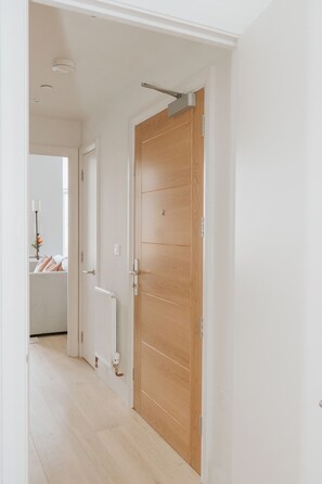 A hallway with a wooden door, a radiator, and a radiator visible in the background. - Premium London Stay – Luxury 1-Bed Apartment (London)