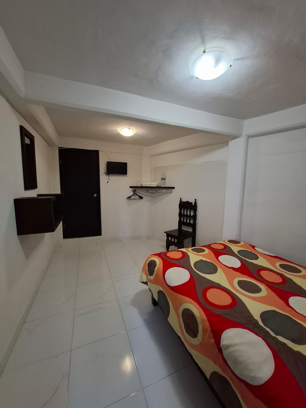 A room with a bed, a chair, a small table, a TV, and a door.