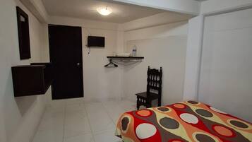 A room with a bed, a chair, a small table, a TV, and a door.