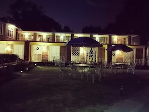 Um edifício com várias janelas e portas, área de estar ao ar livre com guarda-sóis e uma entrada bem iluminada.