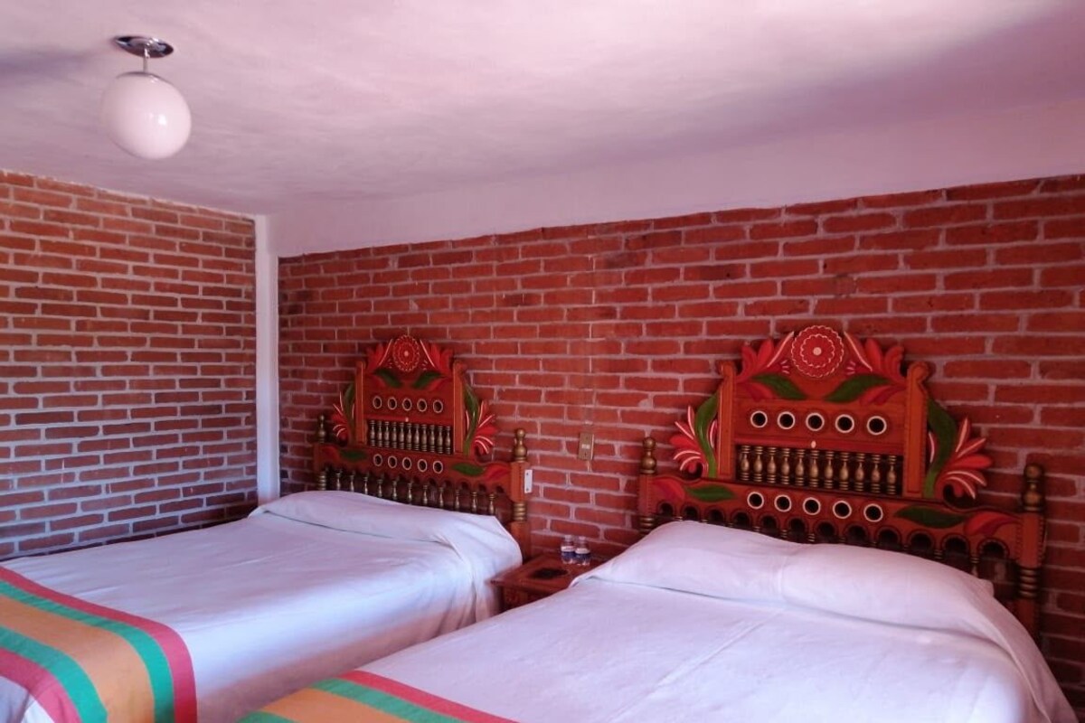 A room with two beds, each with a wooden headboard, a brick wall, and a round ceiling light.