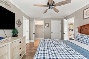 Ein Schlafzimmer mit Bett, Kommode, Deckenventilator und Fernseher an der Wand.