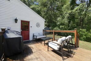 Eine Holzterrasse mit Gartenmöbeln, einem Grill und einer roten Tür.