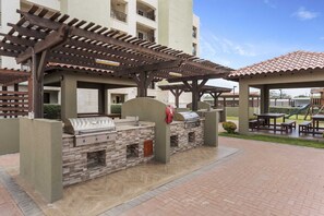 Ein Terrassenbereich im Freien mit Grill, Sitzgelegenheit und einer Pergola.