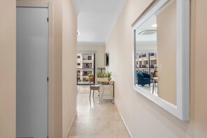 Een gang met uitzicht op een balkon, een tafel met stoelen en een boekenkast.