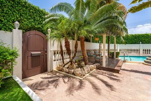 Een privé zwembadgedeelte met een houten poort, palmbomen en een pad van stenen dat leidt naar een zitgedeelte.