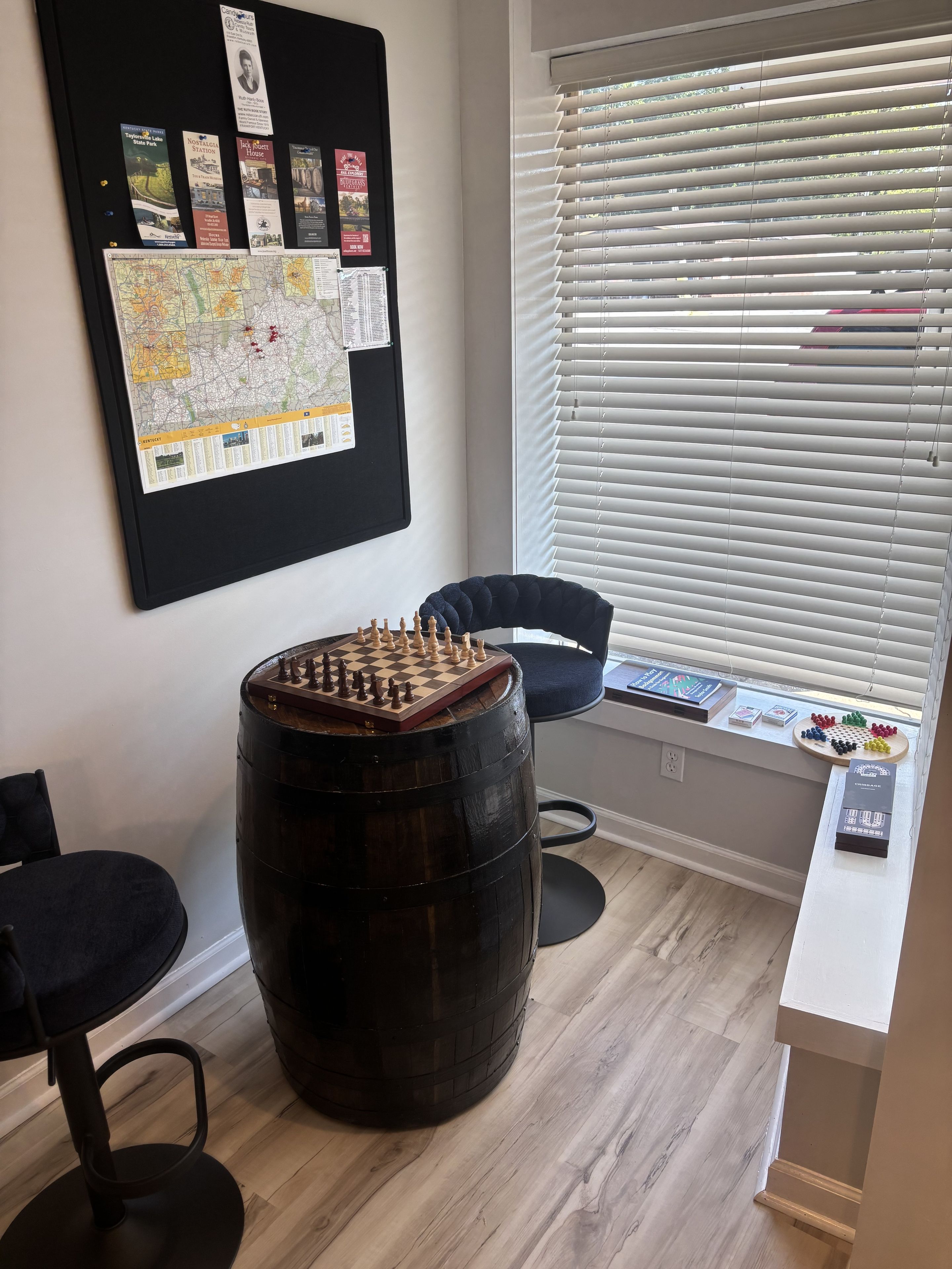 Ett rum med en pall gjord av ett träfat, ett schackbräde, en anslagstavla med diverse papper och ett fönster med persienner.