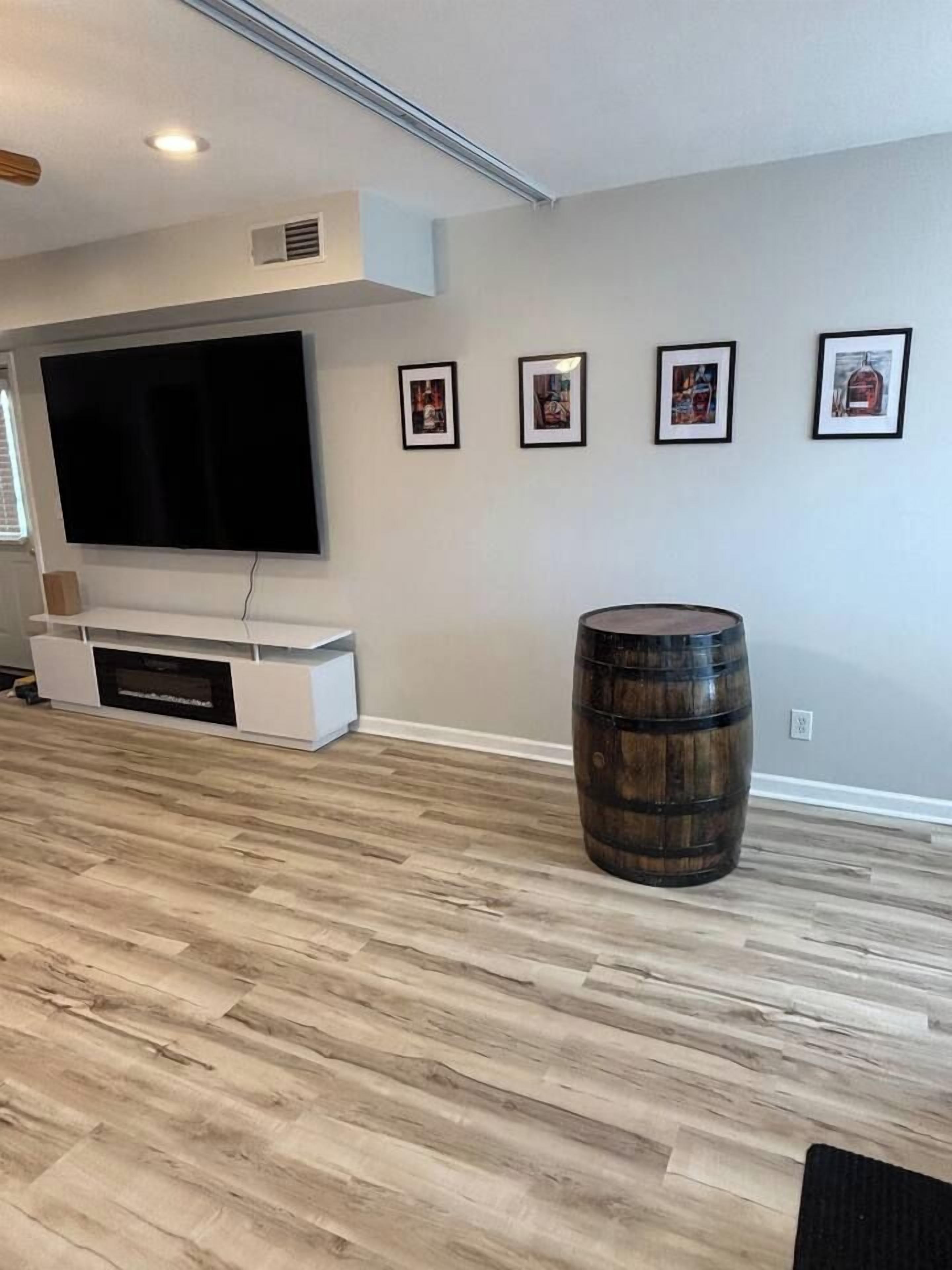 Un salon moderne avec un téléviseur à écran plat, un meuble de rangement blanc, un tonneau en bois et des tableaux encadrés accrochés au mur.