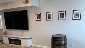 Een moderne woonkamer met een flatscreen televisie, een witte tv-kast, een houten vat en ingelijste foto's aan de muur.