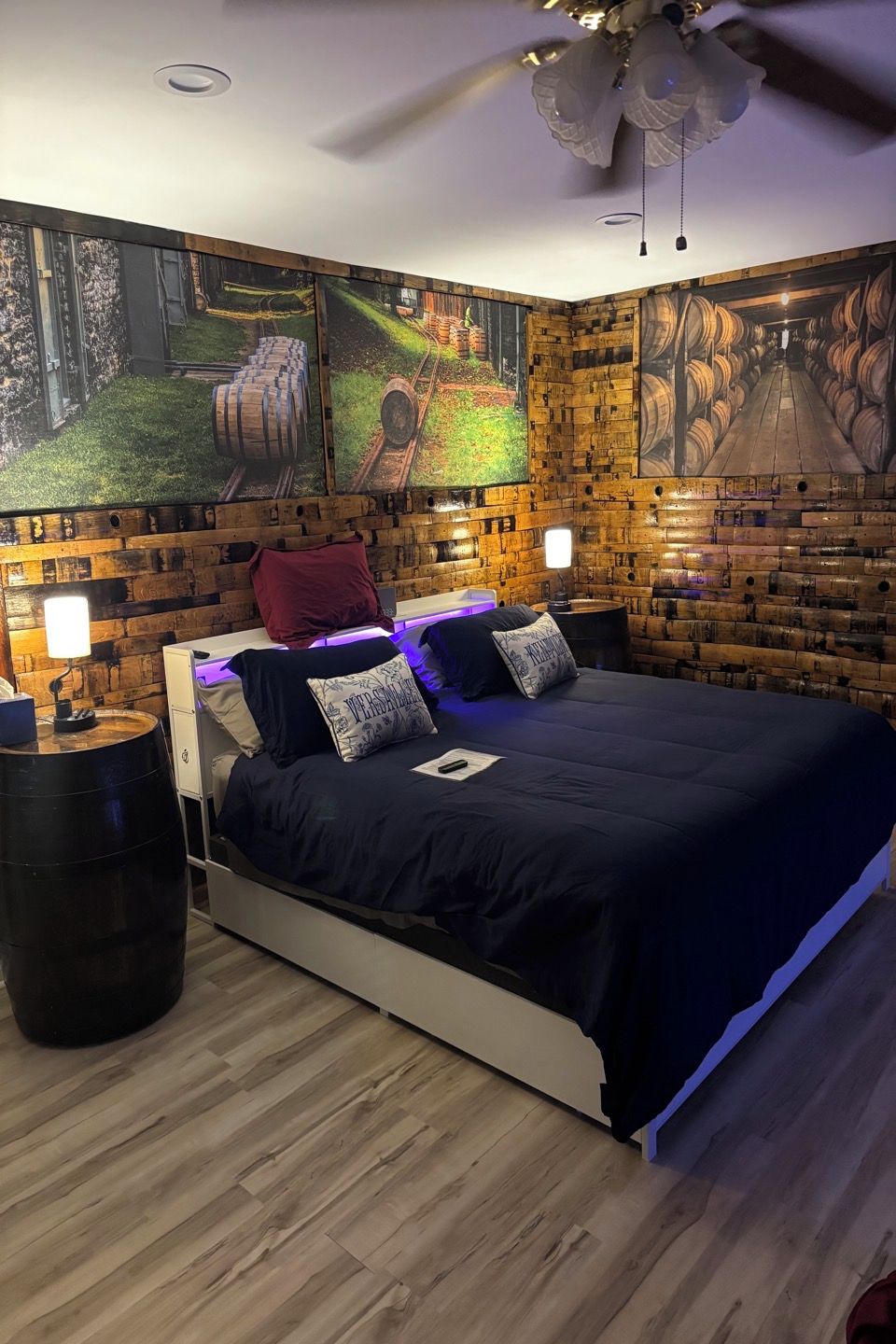 Een slaapkamer met een houten hoofdbord, een bed met blauw beddengoed, twee nachtkastjes met lampen en een plafondventilator.