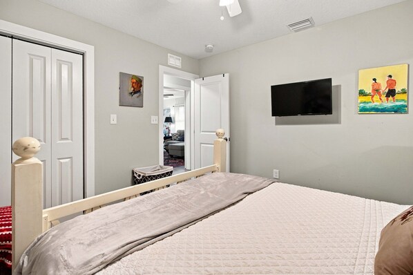 A bedroom with a bed, a television, and a painting on the wall.