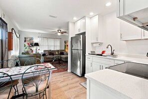 A modern kitchen with white cabinets, a stainless steel refrigerator, and a dining area with a table and chairs.