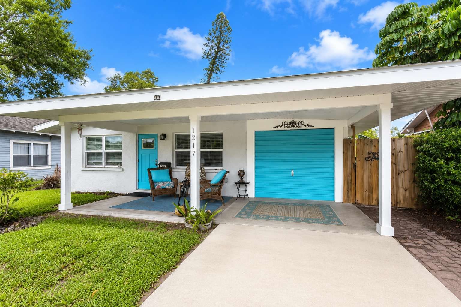 A single-story house with a covered porch, a blue garage door, and a front door with a number plaque.