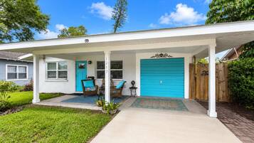 A single-story house with a covered porch, a blue garage door, and a front door with a number plaque.