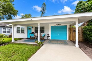 A single-story house with a covered porch, a blue garage door, and a front door with a number plaque.