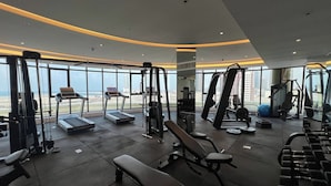 Ein Fitnessstudio mit Laufbändern, Kraftgeräten und Bänken, mit Blick auf die Stadt durch große Fenster.