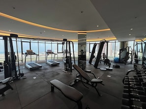 Ein Fitnessstudio mit Laufbändern, Kraftgeräten und Bänken, mit Blick auf die Stadt durch große Fenster.