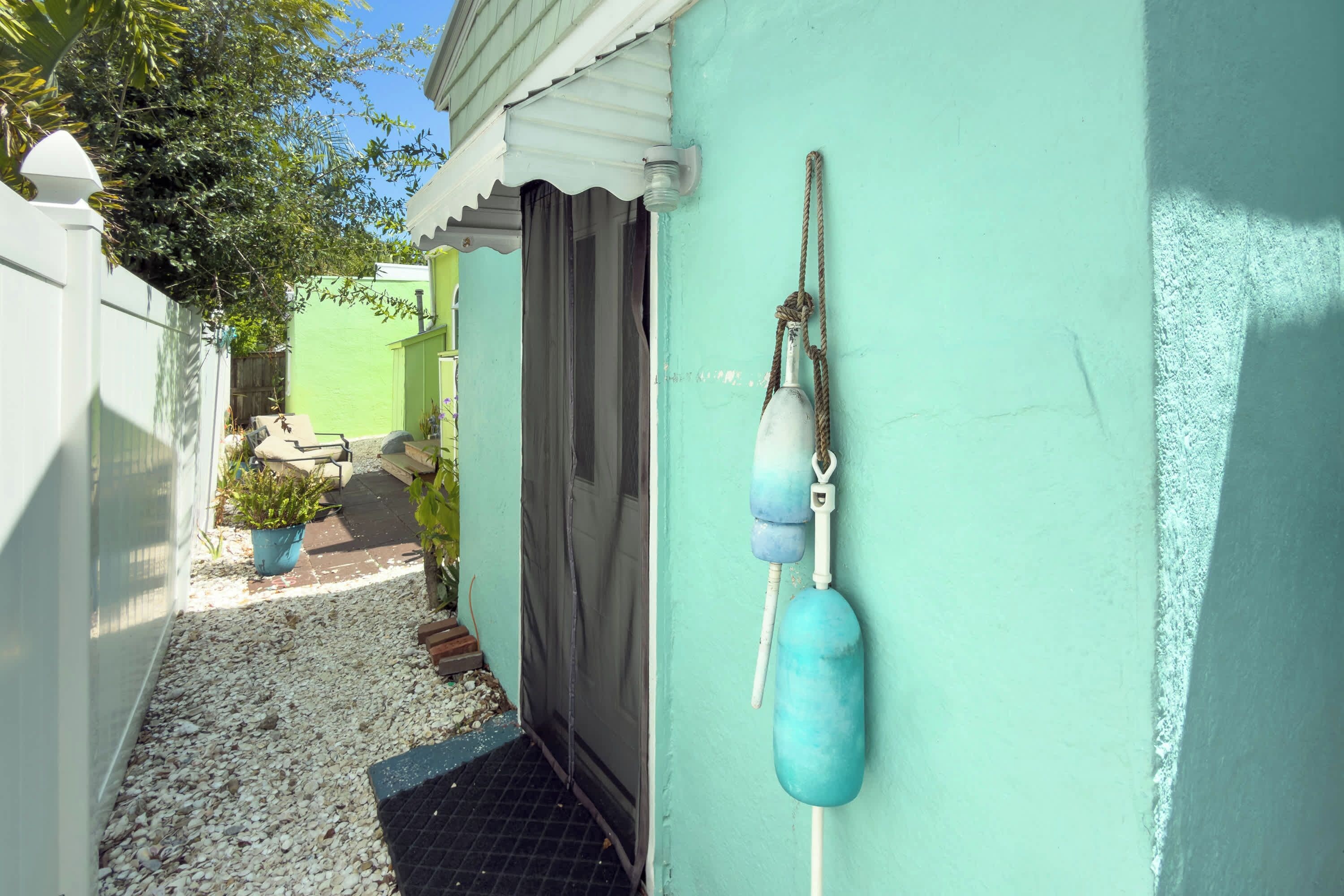 A narrow alleyway with a door, a small garden area with a bench, and a wall-mounted buoy.