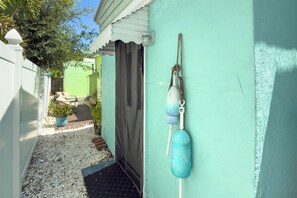 A narrow alleyway with a door, a small garden area with a bench, and a wall-mounted buoy. - Merman  Cave  Studio (Bradenton)