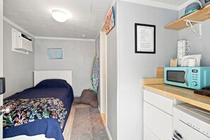 A compact room with a bed, a small kitchenette with a microwave, a framed menu on the wall, and a radiator. - Merman  Cave  Studio (Bradenton)