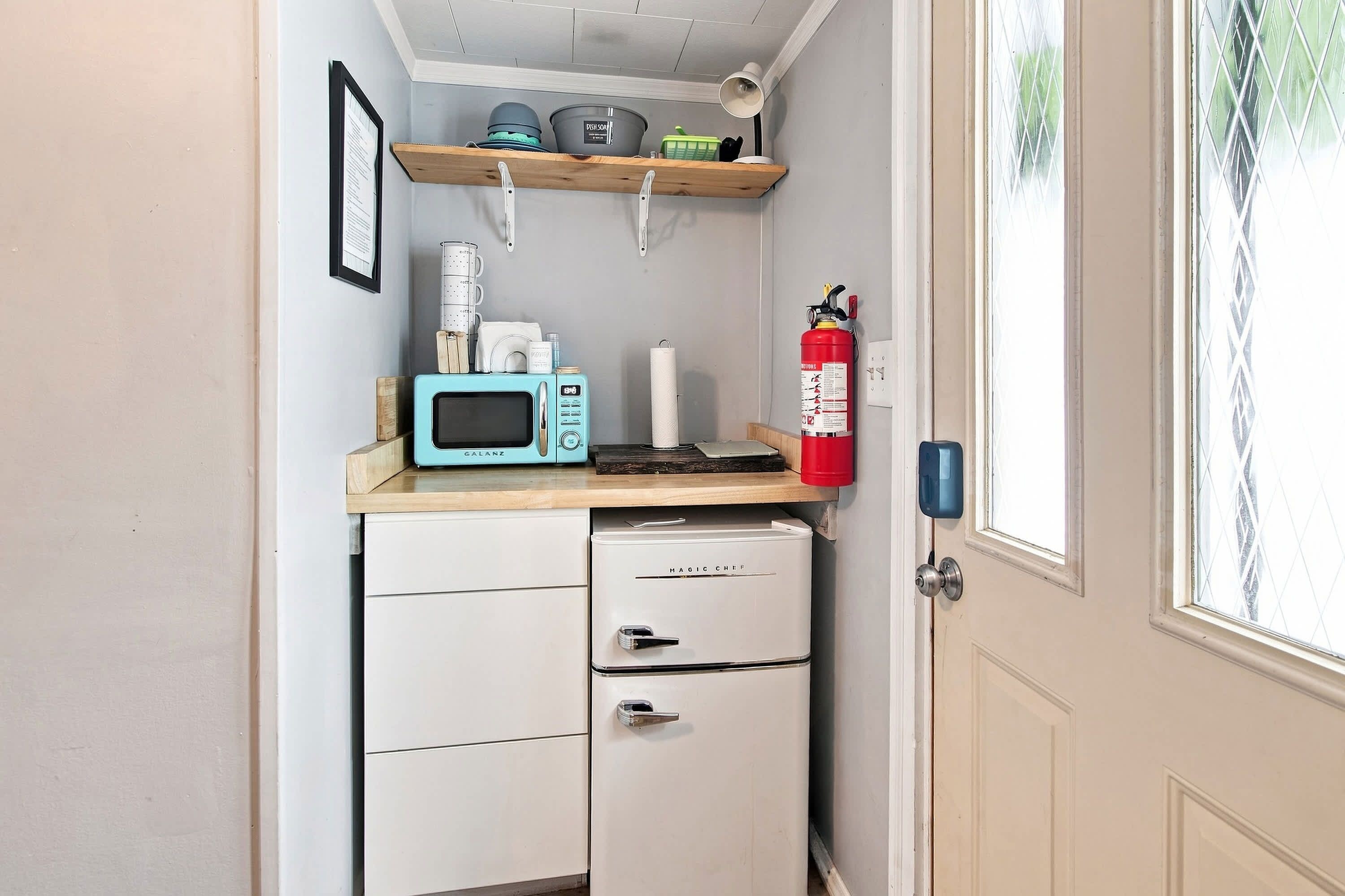 A compact kitchenette with a microwave, a small refrigerator, and a fire extinguisher.