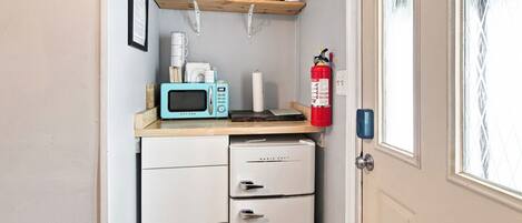 A compact kitchenette with a microwave, a small refrigerator, and a fire extinguisher.