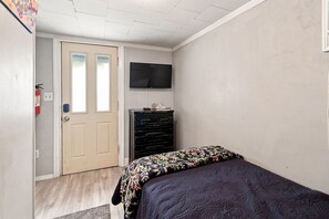 A bedroom with a bed, a dresser, a television on the wall, and a door leading to another room. - Merman  Cave  Studio (Bradenton)