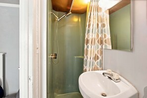 A bathroom with a glass-enclosed shower, a white sink, and a mirror above the sink. - Merman  Cave  Studio (Bradenton)