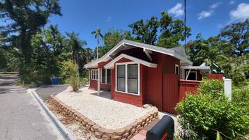 A red single-story house with a front porch, a mailbox, and a gravel driveway.