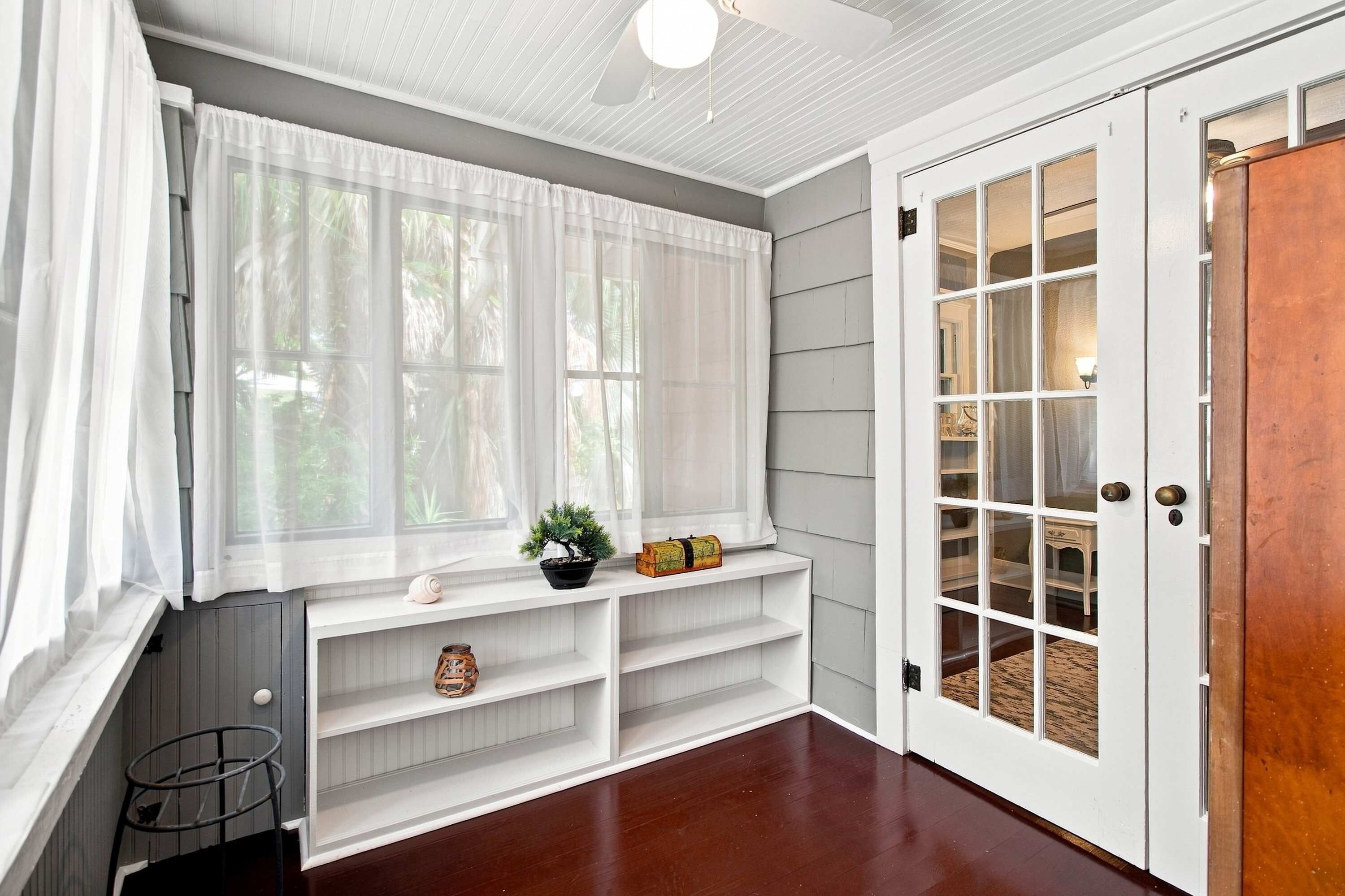 A room with a large window, a white door with glass panels, and a built-in bench with shelves.