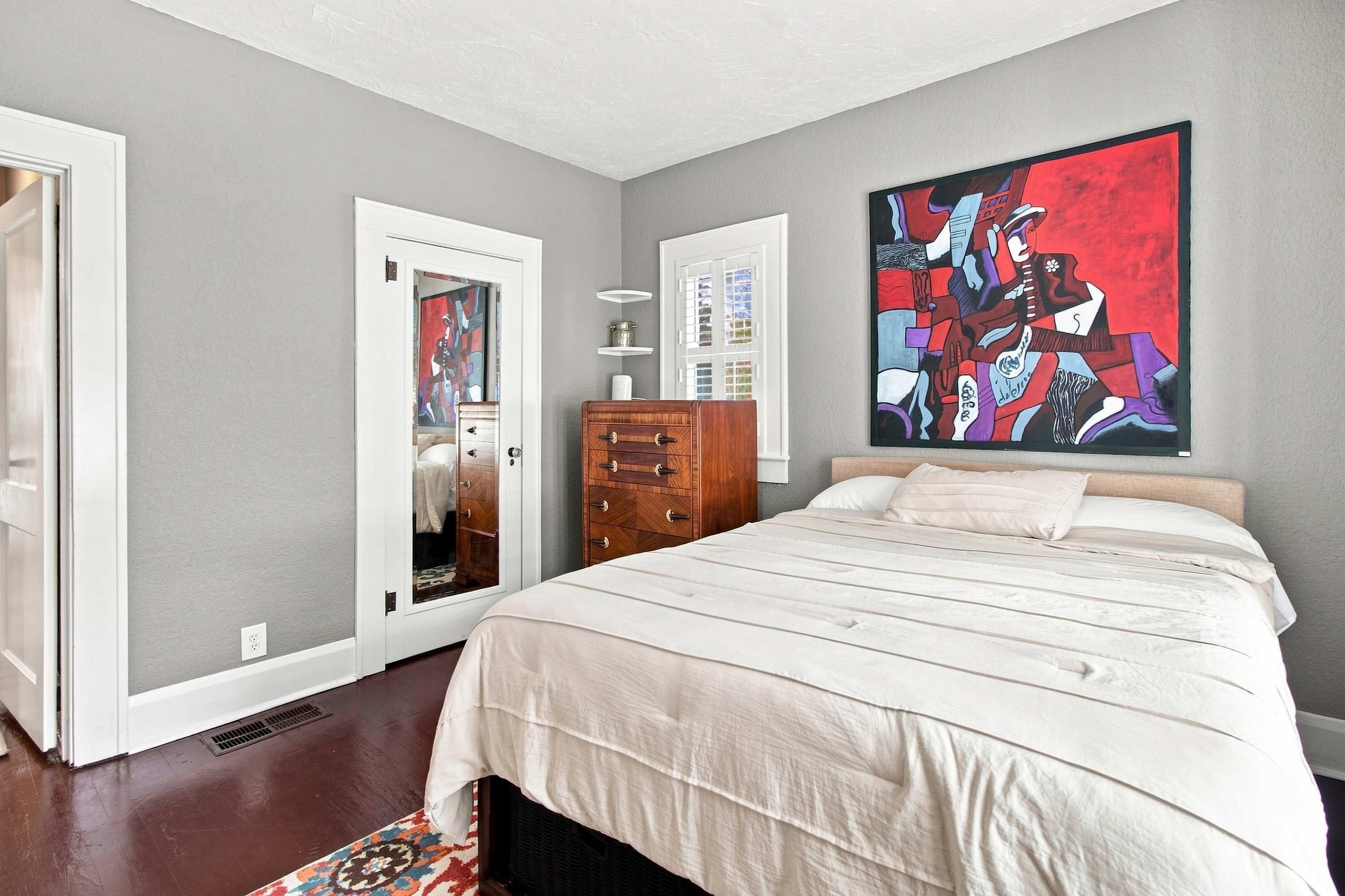A bedroom with a bed, dresser, and a large abstract painting on the wall.