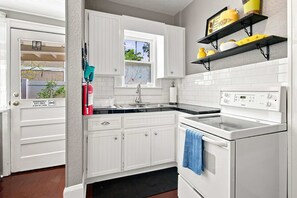 A kitchen with white cabinetry, a stove, and a microwave. There is a window with a view of trees and a door with an emergency exit sign.
