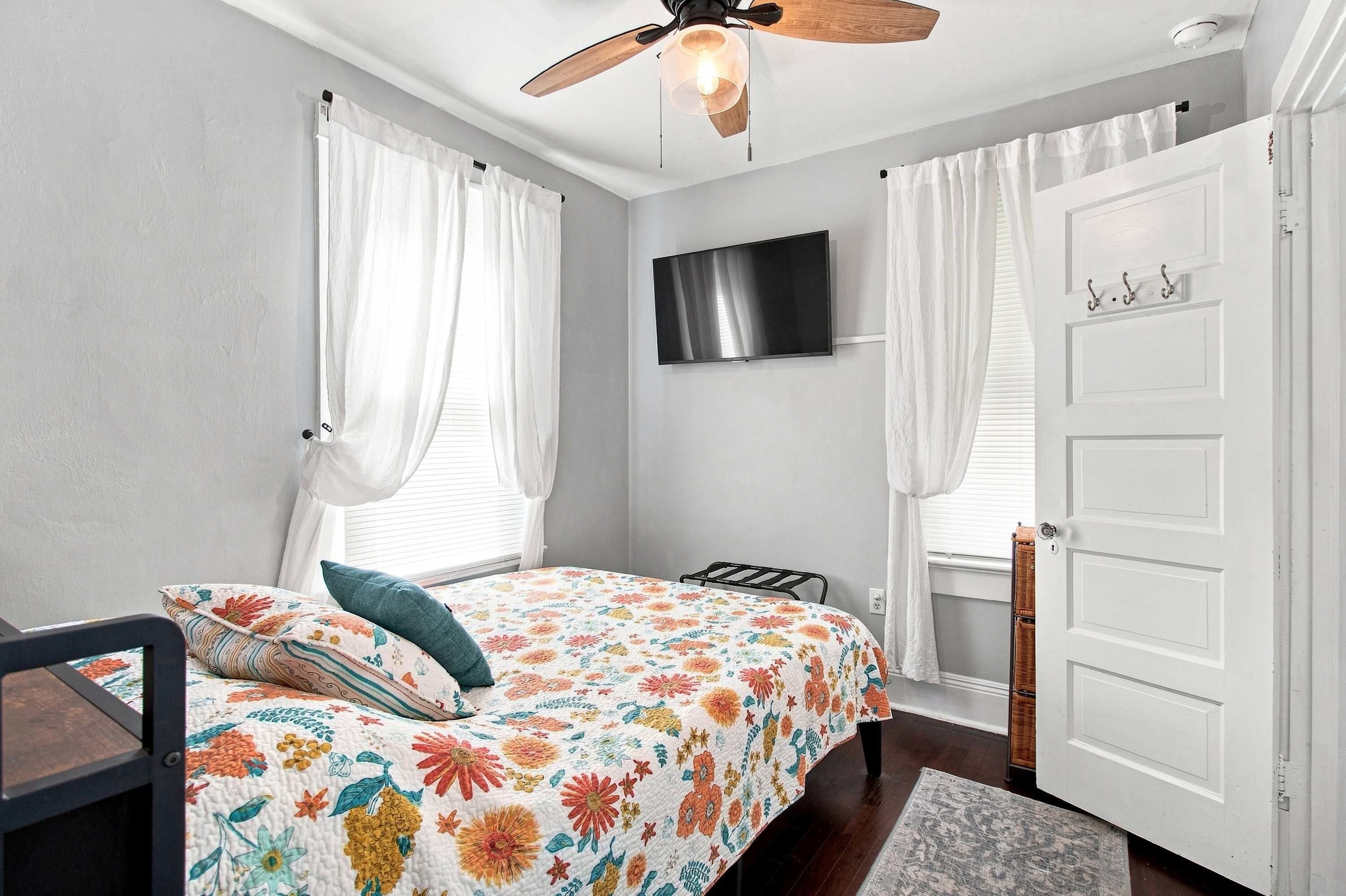 A bedroom with a bed, a ceiling fan, a TV, and a white door.