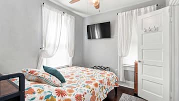 A bedroom with a bed, a ceiling fan, a TV, and a white door.