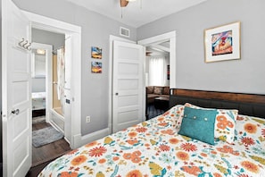 A bedroom with a bed, a door, a hallway, and a painting on the wall. - The Koi House Cottage (Bradenton)
