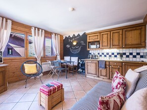 A cozy kitchen with wooden cabinets, a dining area with a table and chairs, and a view through the window. - Bright apartment near the slopes (Les Menuires)