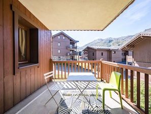 A wooden balcony with a table and chairs, overlooking a mountain landscape. - Bright apartment near the slopes (Les Menuires)