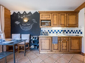 A kitchen with wooden cabinets, a tiled backsplash, and a chalkboard with writing. - Bright apartment near the slopes (Les Menuires)